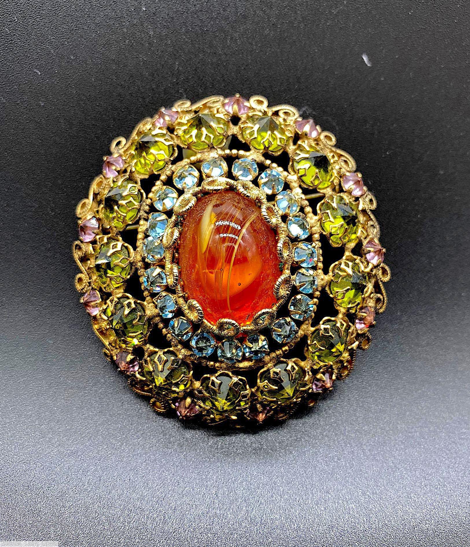 Schreiner 3 rounds radial oval domed radial pin large oval cab center 19 surrounding small inverted stone 2nd round 13 inverted stone outer round 13 stone scrollwork small circle style prong swirled carnelian large oval cab center clear aqua small inverted stone olivine inverted stone clear pink small inverted stone goldtone jewelry