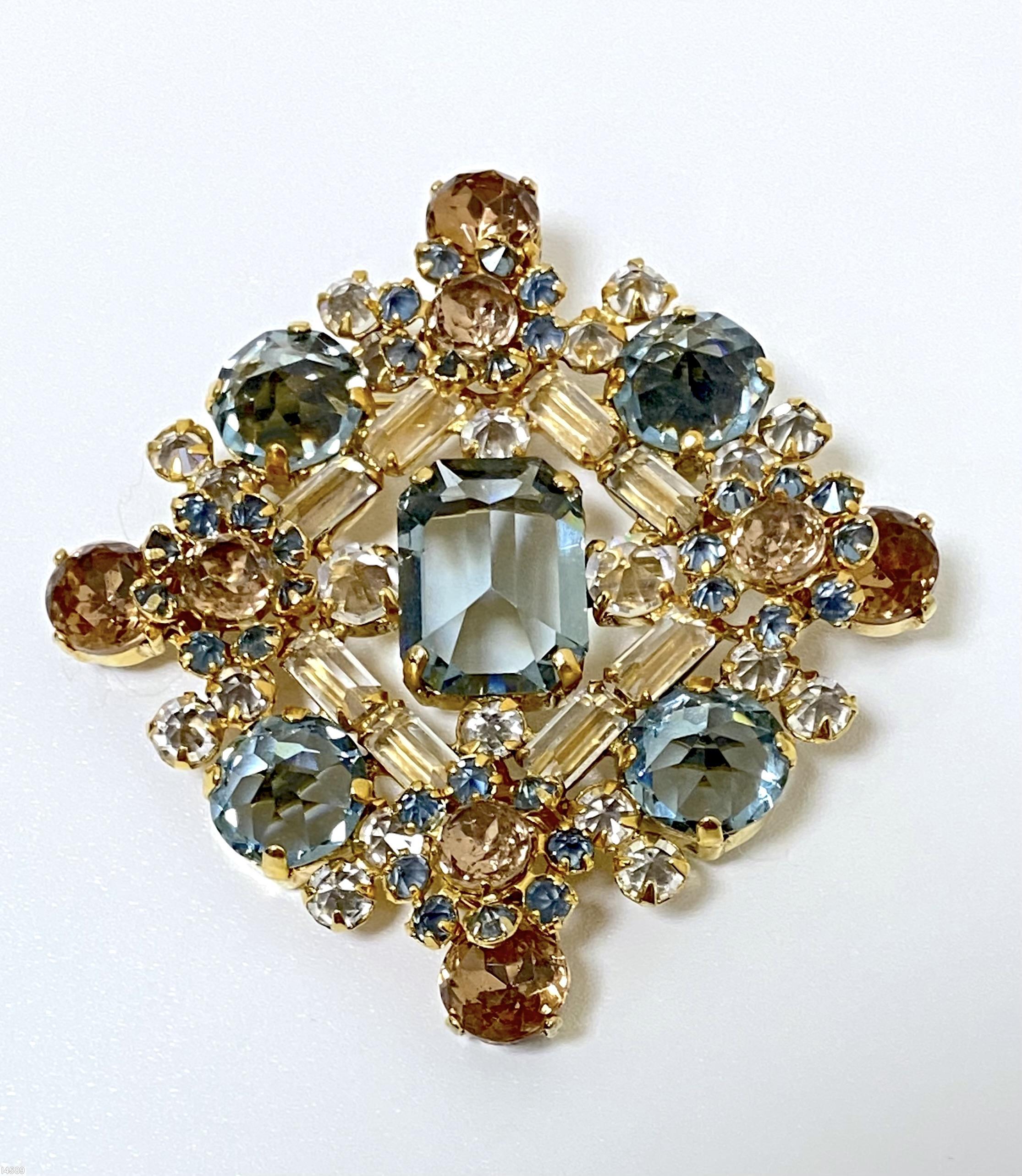 Schreiner diamond shaped radial pin elongated hexagon center stone 4 large round cab 4 flower head of 6 chatons surrounding 1 chaton 8 small baguette 4 small round cab clear champagne small baguette smoky blue large faceted chaton blue small inverted small inverted crystal faceted round topaz goldtone jewelry