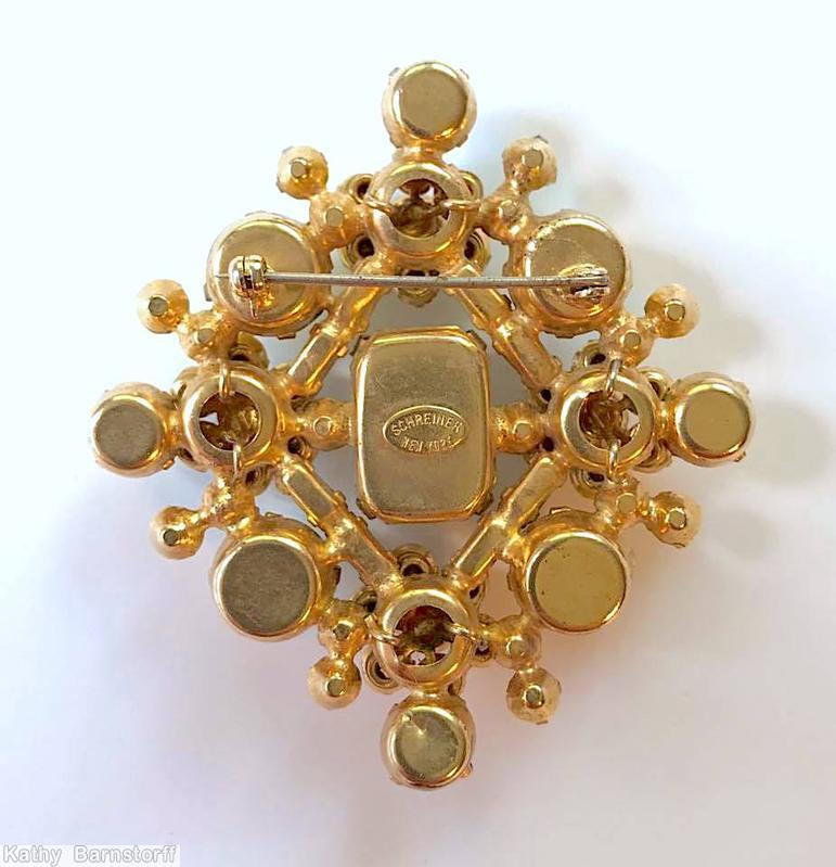 Schreiner diamond shaped radial pin elongated hexagon center stone 4 large round cab 4 flower head of 6 chatons surrounding 1 chaton 8 small baguette 4 small round cab lime round cab navy small buguette milk white chaton goldtone jewelry